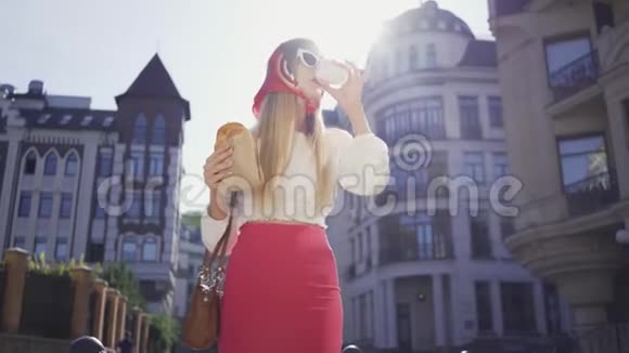 肖像漂亮的年轻女人走在街上喝咖啡吃羊角面包漂亮的时髦女孩视频的预览图
