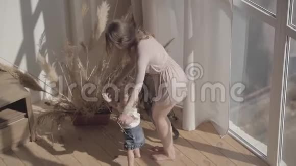 可爱的女人和她的女婴站在家里的地板上孩子迈出第一步妈妈支持她妈妈玩游戏视频的预览图