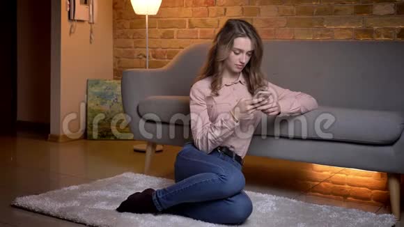 年轻女学生坐在地板上看手机在舒适的家庭氛围中平静地反应的肖像视频的预览图