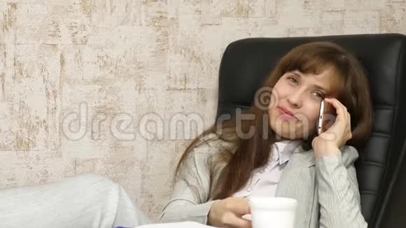 女商人坐在椅子上光着脚在桌子上放松喝茶喝咖啡在办公室工作的女孩视频的预览图