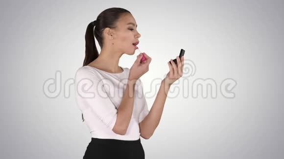 美丽的女人把嘴唇涂上粉红色的唇膏看着镜子的渐变背景视频的预览图