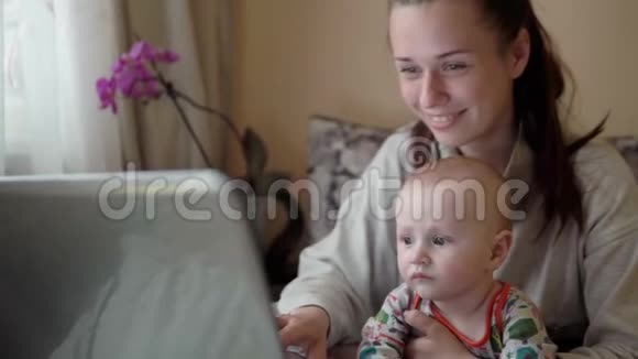 休产假的年轻母亲在家工作抱着婴儿坐在笔记本电脑前视频的预览图