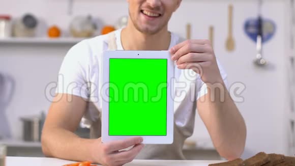 笑容可掬的男子在相机上显示绿色屏幕平板电脑在线烹饪课程视频的预览图
