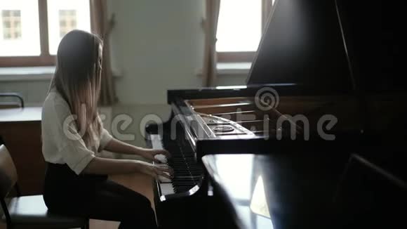 女人在窗户的背景上缓慢地弹着黑色的钢琴视频的预览图