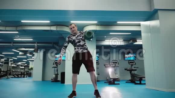 肌肉男在明亮的健身房中缓慢地举起沉重的水壶铃视频的预览图