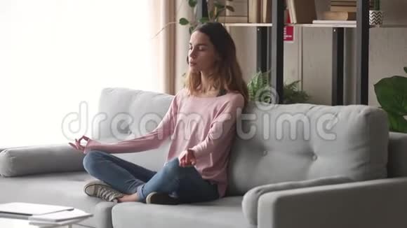 宁静的女孩坐在沙发上做瑜伽呼吸锻炼视频的预览图