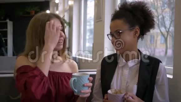 混血女孩的秘密快乐的非裔美国少女说与白人女朋友耳语与杯子视频的预览图