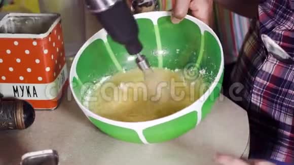 人类用电动搅拌器将快速的鸡蛋混合在绿色的大碗里视频的预览图