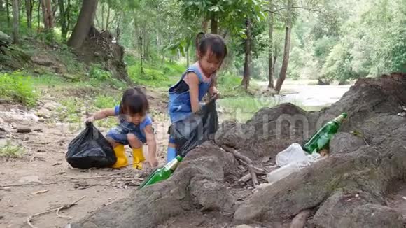 亚洲的小孩子正在公共河边捡垃圾和塑料瓶装在黑色的袋子里视频的预览图
