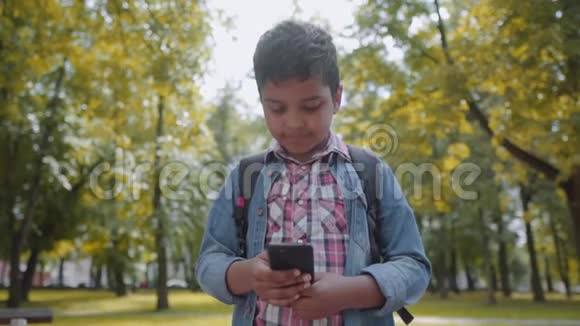 户外肖像美国快乐学校男孩与智能手机年轻的学生看着手机回到学校视频的预览图