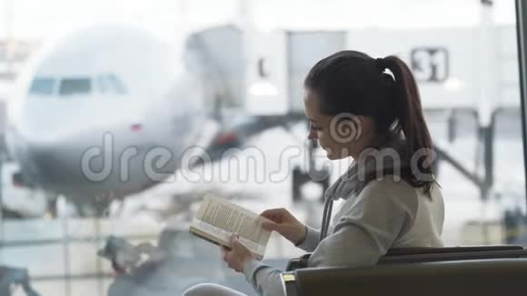 美丽的旅行女孩坐在机场休息室喝饮料带走咖啡在飞机背景上看书视频的预览图