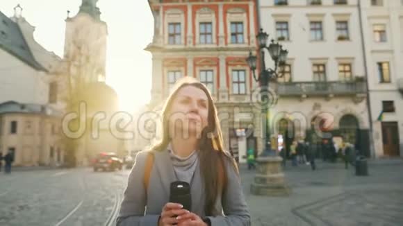 女人手里拿着一个保温杯走在街上欣赏日落时分的古城建筑视频的预览图