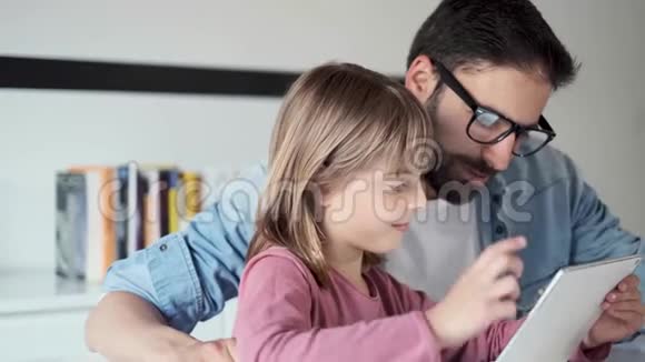 英俊的年轻父亲和他的女儿在家里用数码平板电脑视频的预览图