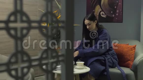 穿着蓝色长袍的女人把茶倒在杯子里女人坐在豪华房间的沙发上泛右视频的预览图