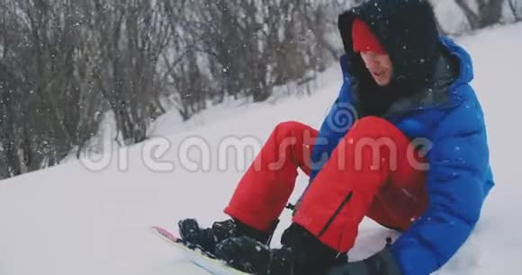 一个穿着红裤子的人坐在雪地上在滑雪坡上系着滑雪板靴视频的预览图