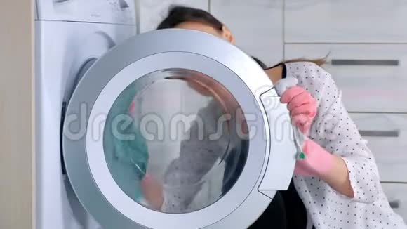 女人戴着粉红色橡胶手套用布洗洗衣机坐在地板上侧视特写视频的预览图