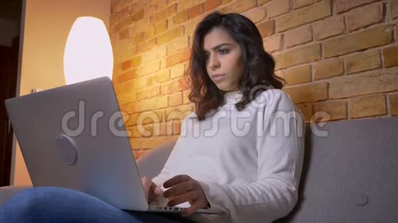 严肃的白种人黑发女商人坐在沙发上用笔记本电脑专心工作的肖像视频的预览图