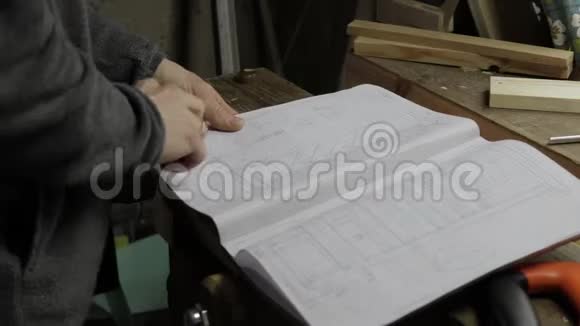 男木匠检查笔记本上的木制建筑蓝图显示其中一些并解释细节视频的预览图