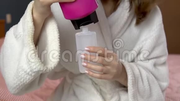 一个女人把洗发水倒进一个小罐子里穿浴袍的女人拿着一罐旅行洗发水视频的预览图