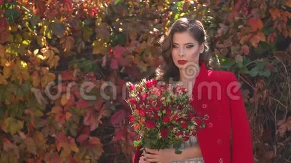 在秋天的公园里穿着一件连衣裙和一件红色外套的女孩带着一束花视频的预览图