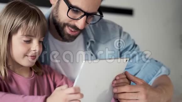 英俊的年轻父亲和他的女儿在家里用数码平板电脑视频的预览图