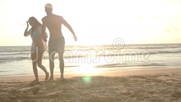 年轻的幸福夫妇在海滩上散步在日落时牵手一男一女出海视频的预览图