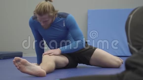 专业人士坐在地板上在健身房伸腿视频的预览图