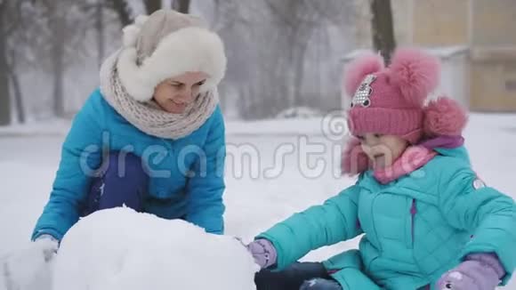 妈妈和她的小女儿在冬天玩得很开心在街上堆雪人视频的预览图