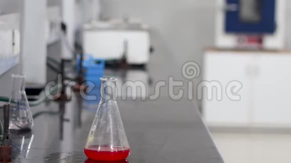 一位科学家把一种无色化学物质从试管中倒入锥形瓶中的红色化学物质的手视频的预览图