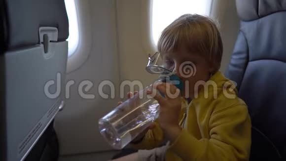 一个小男孩坐在椅子上喝可重复使用的塑料瓶里的水的慢镜头视频的预览图