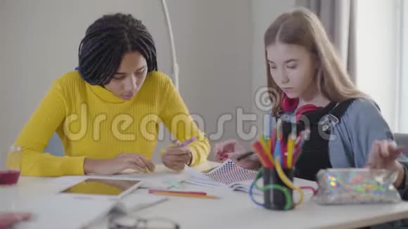 两个女学生做作业的肖像白人和非裔美国女孩坐在桌子旁写字视频的预览图