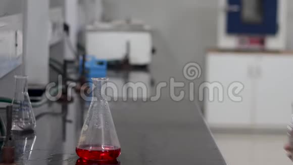一位科学家把一种无色的化学物质从瓶子中倒入锥形瓶中的红色化学物质的手视频的预览图
