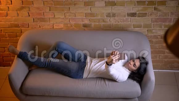 漂亮的黑发女商人在沙发上放松在家里很高兴地在智能手机上制作自拍照片视频的预览图