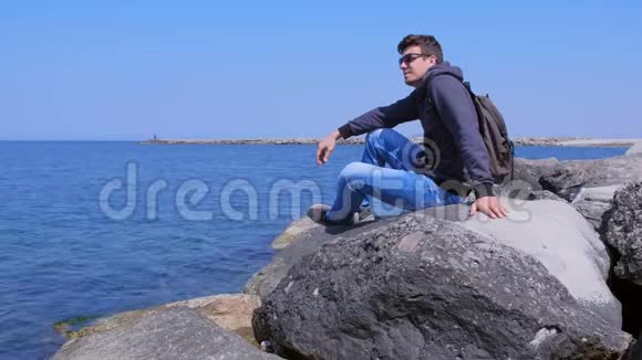 年轻的旅行者欣赏海景坐在海边的巨大石头上视频的预览图