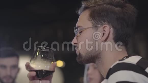 一个英俊的留胡子的年轻男子带着品酒杯的肖像一个男人在昂贵的酒杯里喝酒视频的预览图