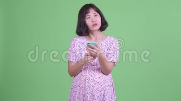 快乐的亚洲孕妇一边思考一边打电话视频的预览图