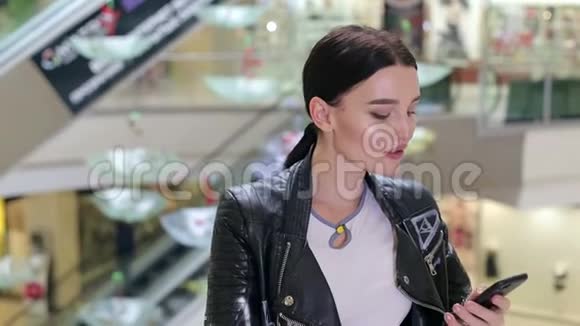 一个穿着皮夹克的女孩在购物中心接电话视频的预览图