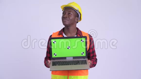 年轻快乐的非洲男子建筑工人一边思考一边展示笔记本电脑视频的预览图
