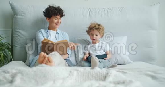 母亲看书而孩子则在床上使用平板电脑视频的预览图