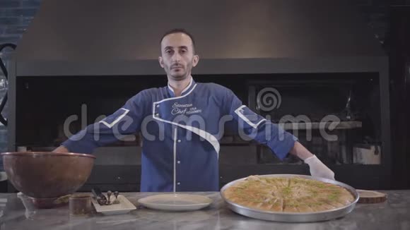 一位自信成功的厨师穿着蓝色制服站在厨房里一道美味可口的菜肴旁边的肖像视频的预览图
