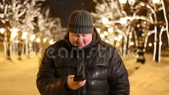 一个英俊的黑人胖子的画像是在冬天的城市街道晚上用他的电话视频的预览图