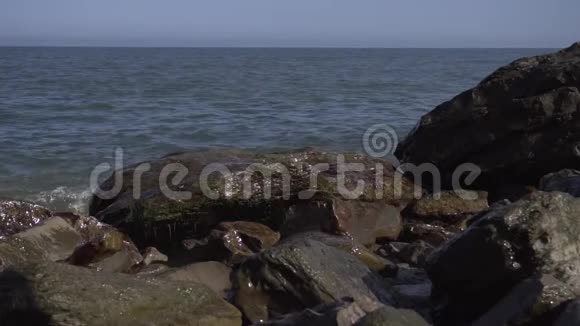 阳光明媚的自然风光潮湿的棕色岩石在海岸与下降的海浪视频的预览图