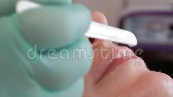 一个戴手套的美容师把凝胶放在一个漂亮女孩性感的嘴唇上超级特写可爱的女人和视频的预览图
