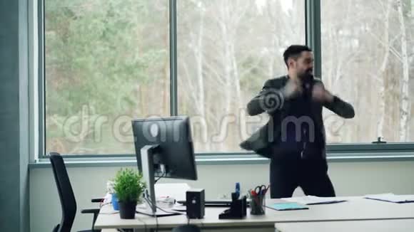 有胡子的商人正在表达积极的情绪跳舞脱下夹克从桌子上扔文件同时还在跳舞视频的预览图