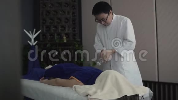 在中国的按摩中一个亚洲人在毛巾下倒液体视频的预览图