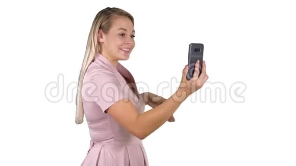 穿着粉色裙子的女性在白色背景下用她的智能手机打视频电话视频的预览图