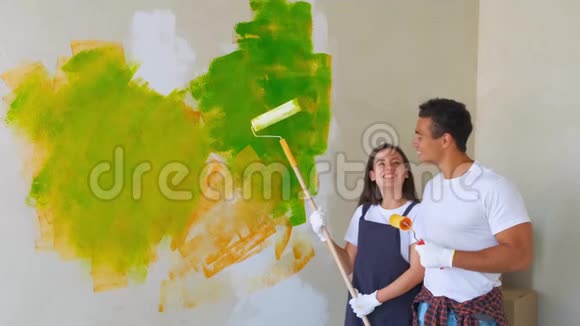笑着一对夫妇把他们的房子画成绿色摆在一堵半完工的墙前上面有一个滚筒和一个浴缸视频的预览图