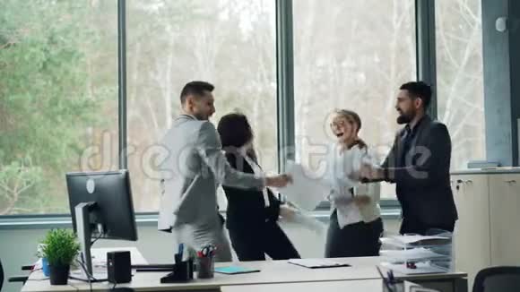 一群快乐的同事在办公室里跳舞在聚会上庆祝公司的活动扔报纸笑和笑视频的预览图