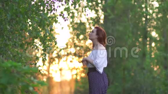 红发女人穿着裤子和白色衬衫摆姿势日落乡村公路与美丽的傍晚阳光绿色视频的预览图