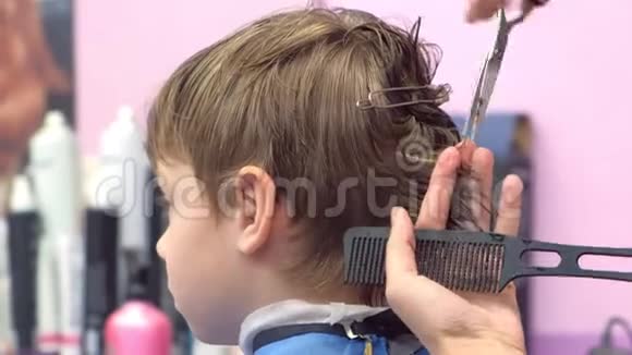 理发师用剪刀在男孩头上剪头发后景造型师手特写视频的预览图